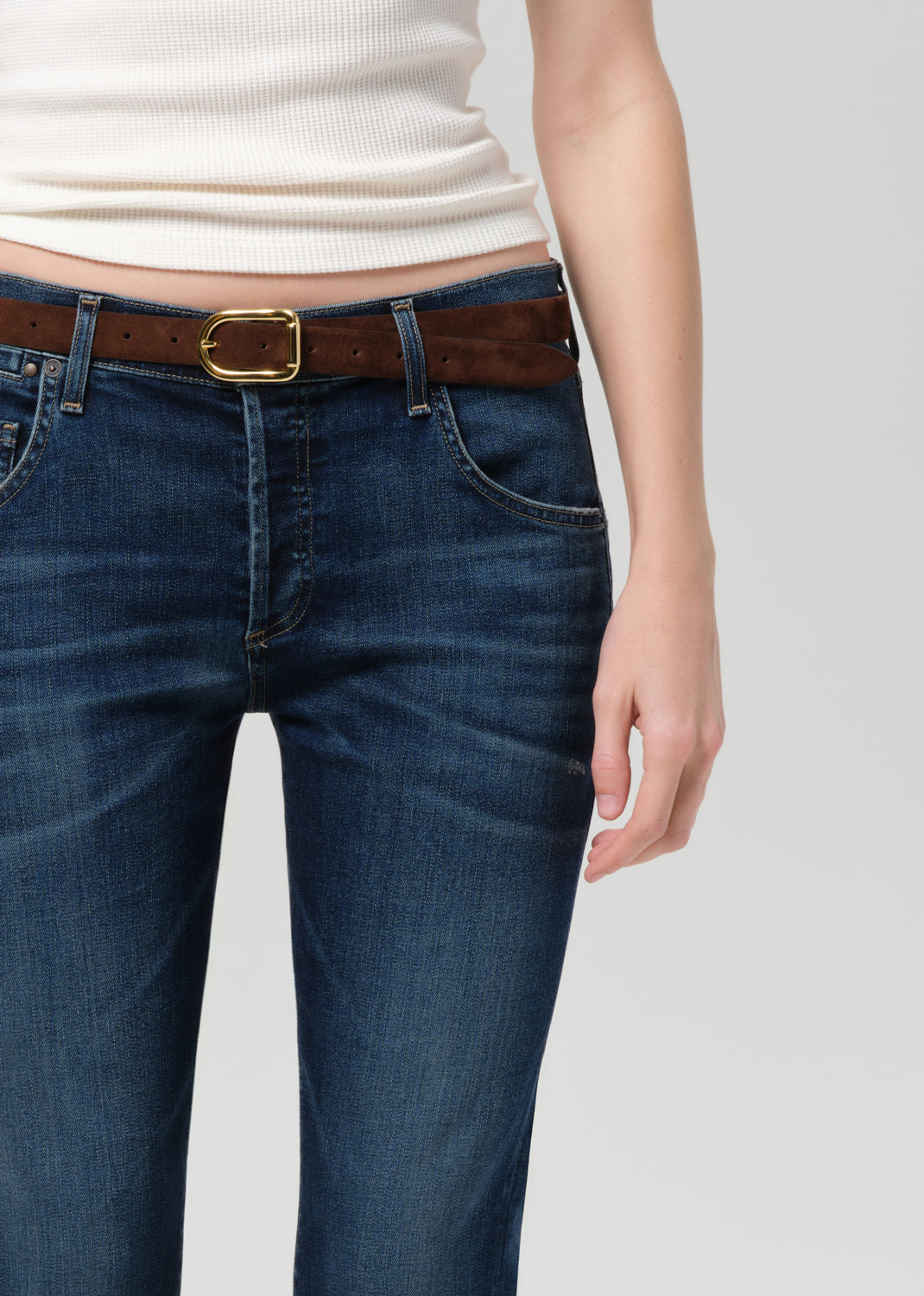 Person wearing blue jeans and a white top on a plain background