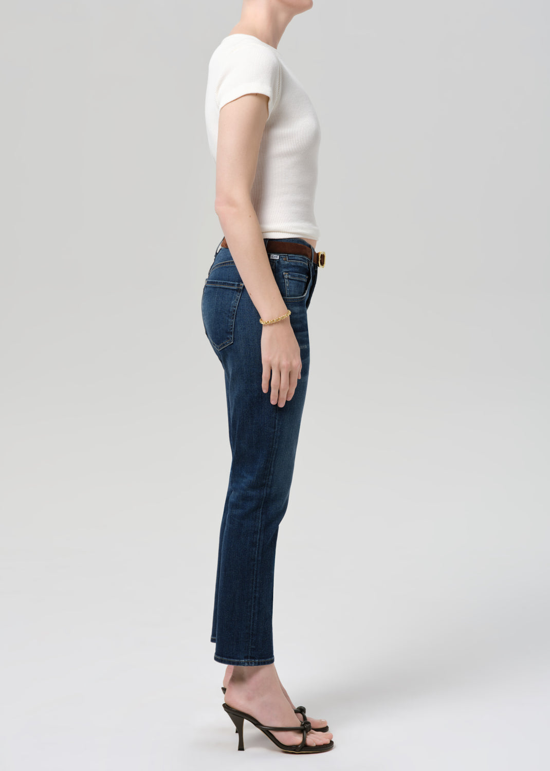 Person wearing blue jeans and a white top on a plain background