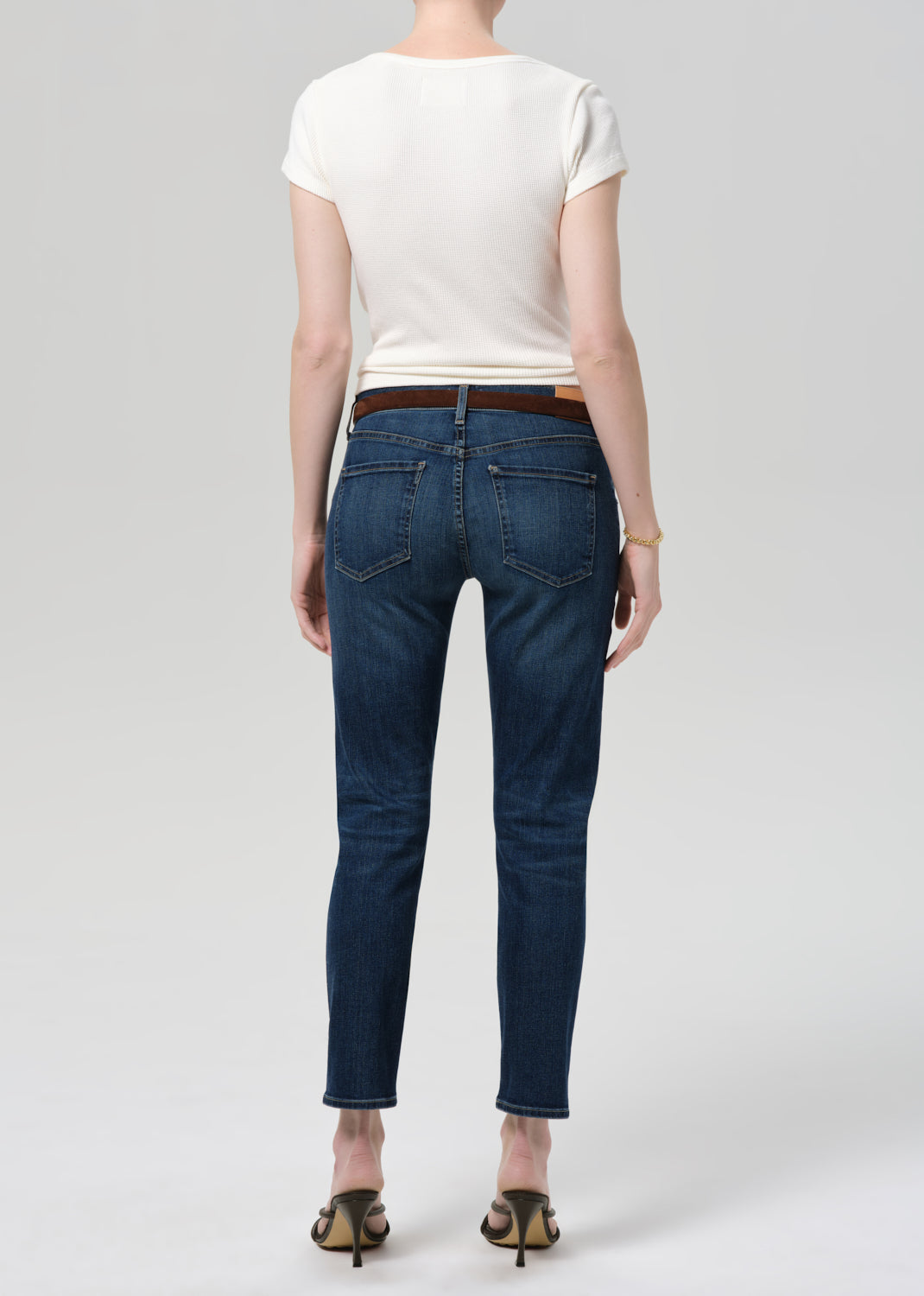 Person wearing blue jeans and a white top on a plain background