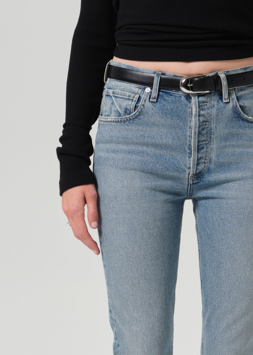 Close up of person wearing a black belt and blue pants on a grey background