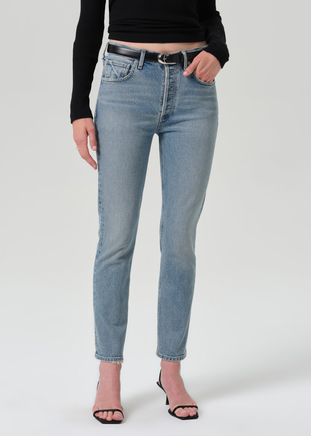 Person wearing black long sleeve top with blue pants on a grey background