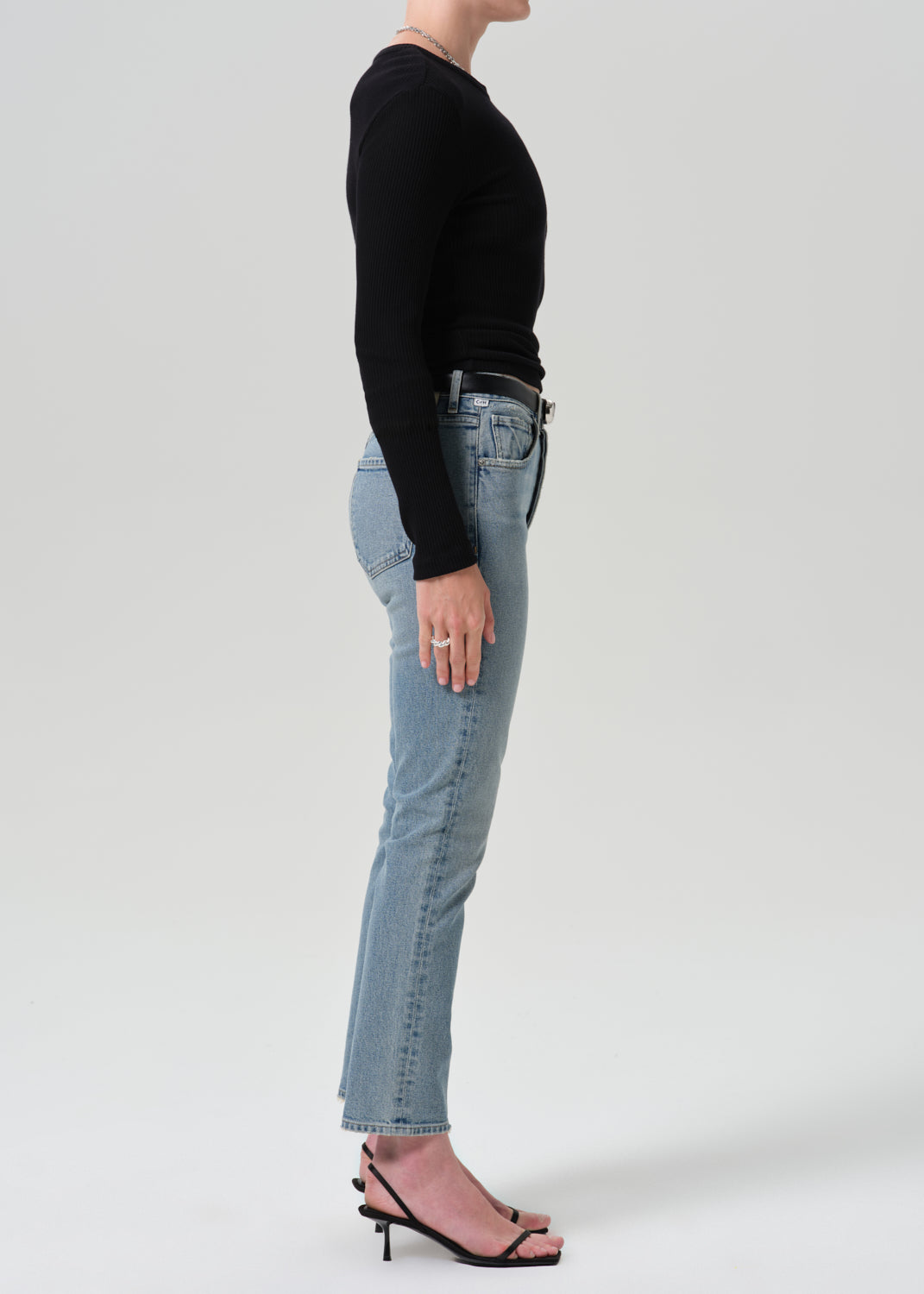 Person wearing black long sleeve top with blue pants on a grey background