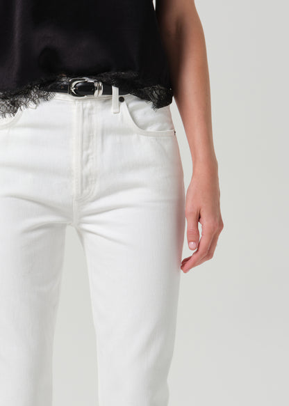 Close-up of a person wearing white jeans with a black top and a black belt with a silver buckle, against a grey background.