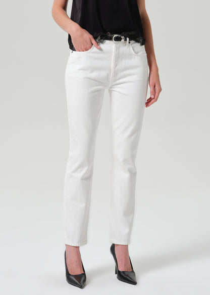 White slim-fit jeans worn by a model, styled with a black belt, black top, and black pointed-toe heels against a grey background.