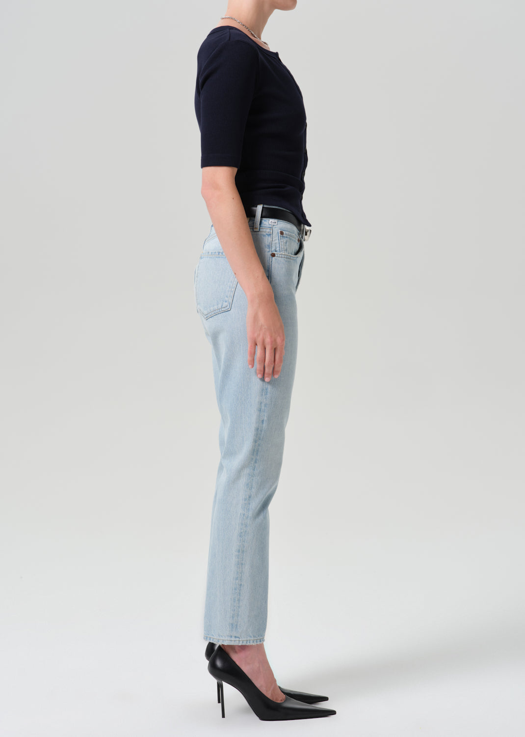 Person wearing navy cardigan with light blue pants on a grey background