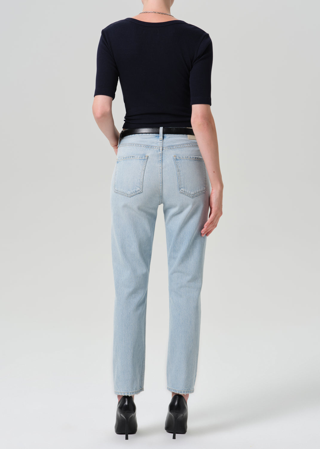 Person wearing navy cardigan with light blue pants on a grey background