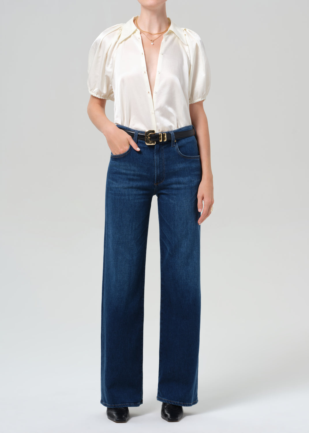 Person wearing a white blouse and blue jeans on a plain background