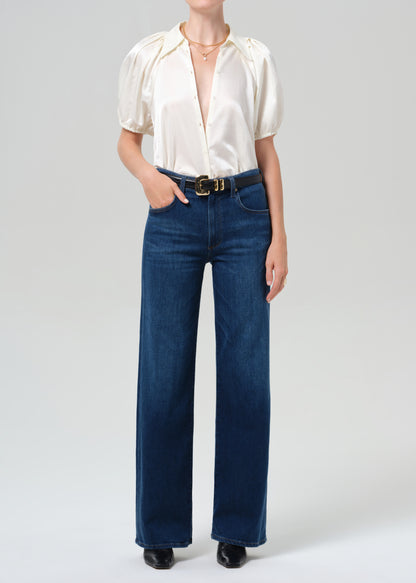 Person wearing a white blouse and blue jeans on a plain background