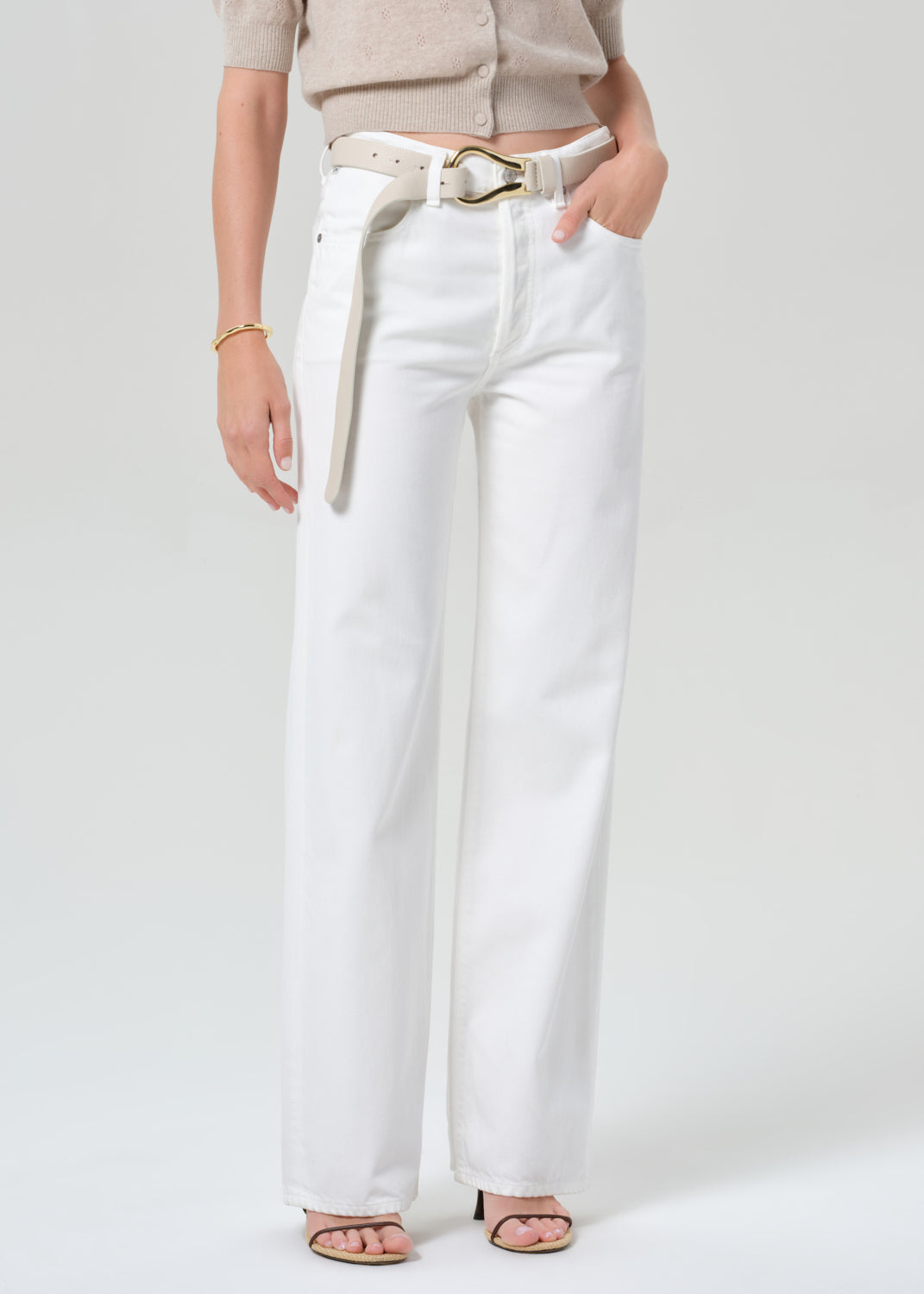 Person wearing a beige cardigan and white jeans on a plain background