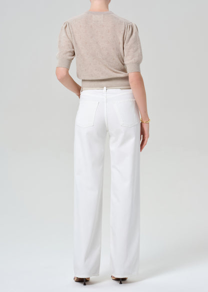 Person wearing a beige cardigan and white jeans on a plain background