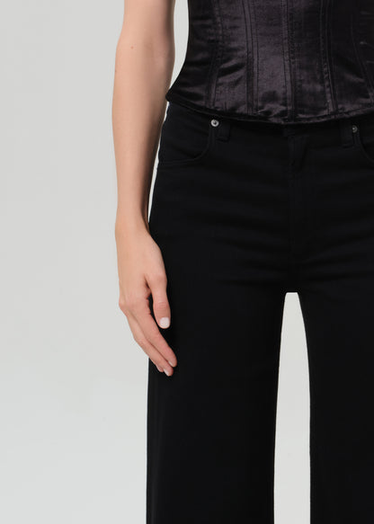 Person wearing a black corset top and black pants on a grey background