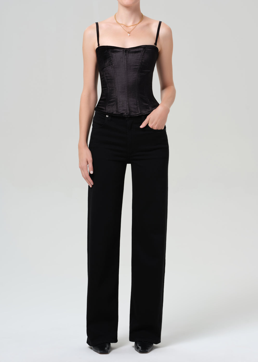 Person wearing a black corset top and black pants on a grey background