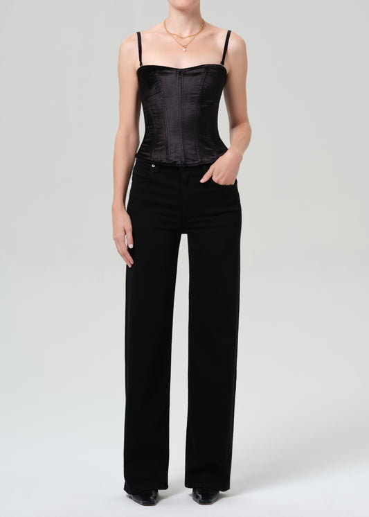 Person wearing a black corset top and black pants on a grey background