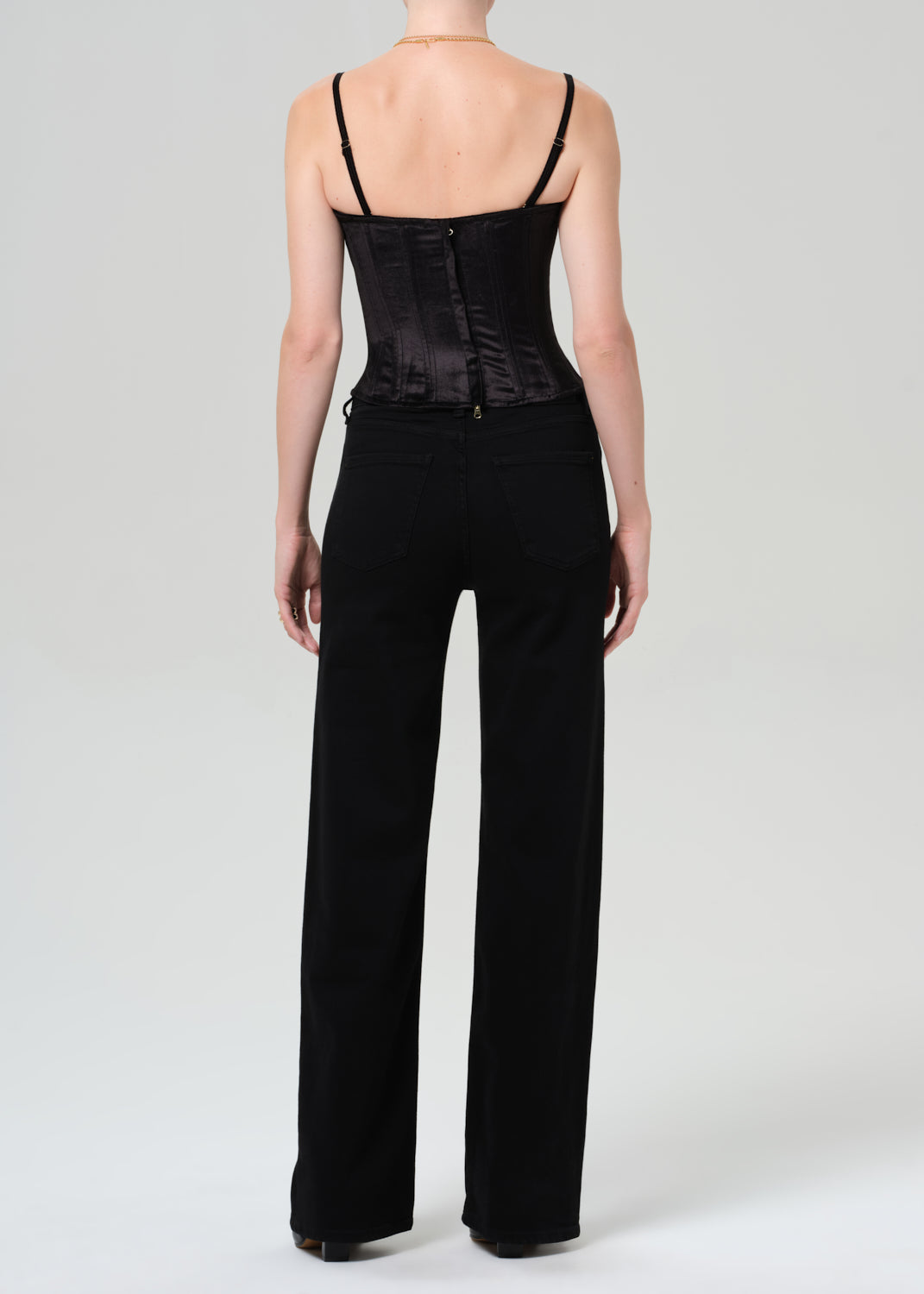 Person wearing a black corset top and black pants on a grey background