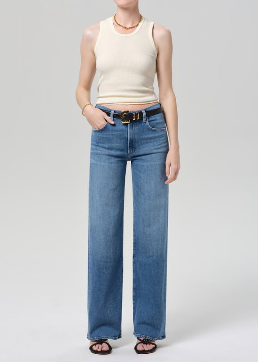 Person wearing a cream ribbed tank and blue jeans on a light gray background