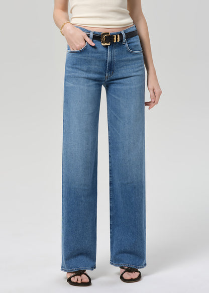 Person wearing a cream ribbed tank and blue jeans on a light gray background