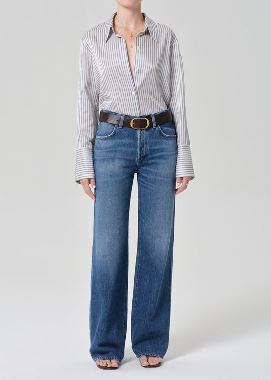 Person wearing a striped shirt and blue jeans on a grey background