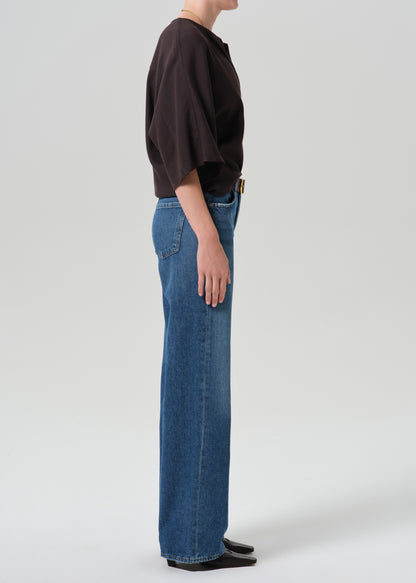 A model shown from the side profile wearing a dark brown cropped t-shirt and wide-leg blue denim jeans against a grey background.