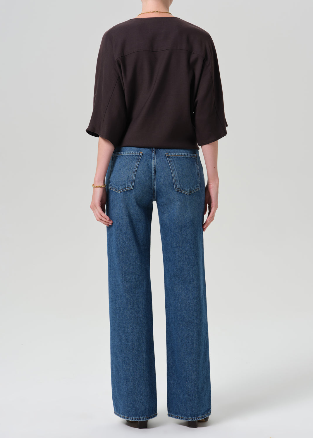 A model shown from the back wearing a dark brown short-sleeve top and wide-leg blue denim jeans, photographed against a grey background.
