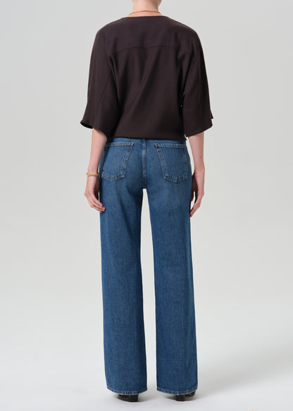 A model shown from the back wearing a dark brown short-sleeve top and wide-leg blue denim jeans, photographed against a grey background.
