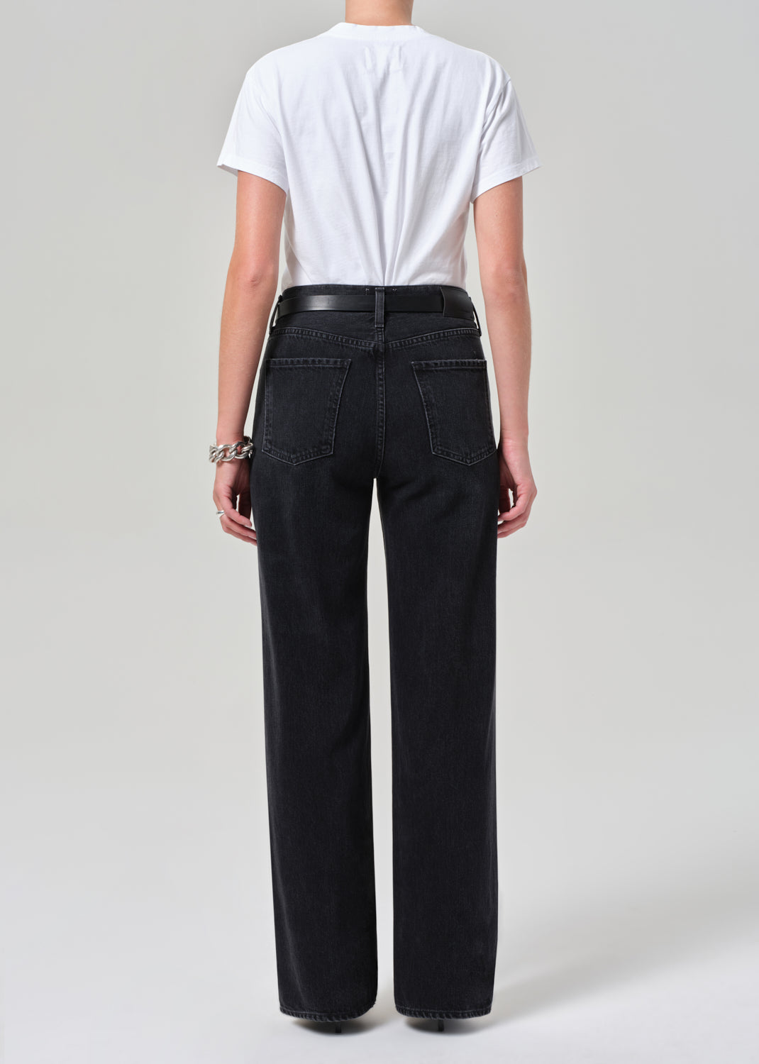 Person wearing black high-waisted jeans and a white t-shirt on a plain background