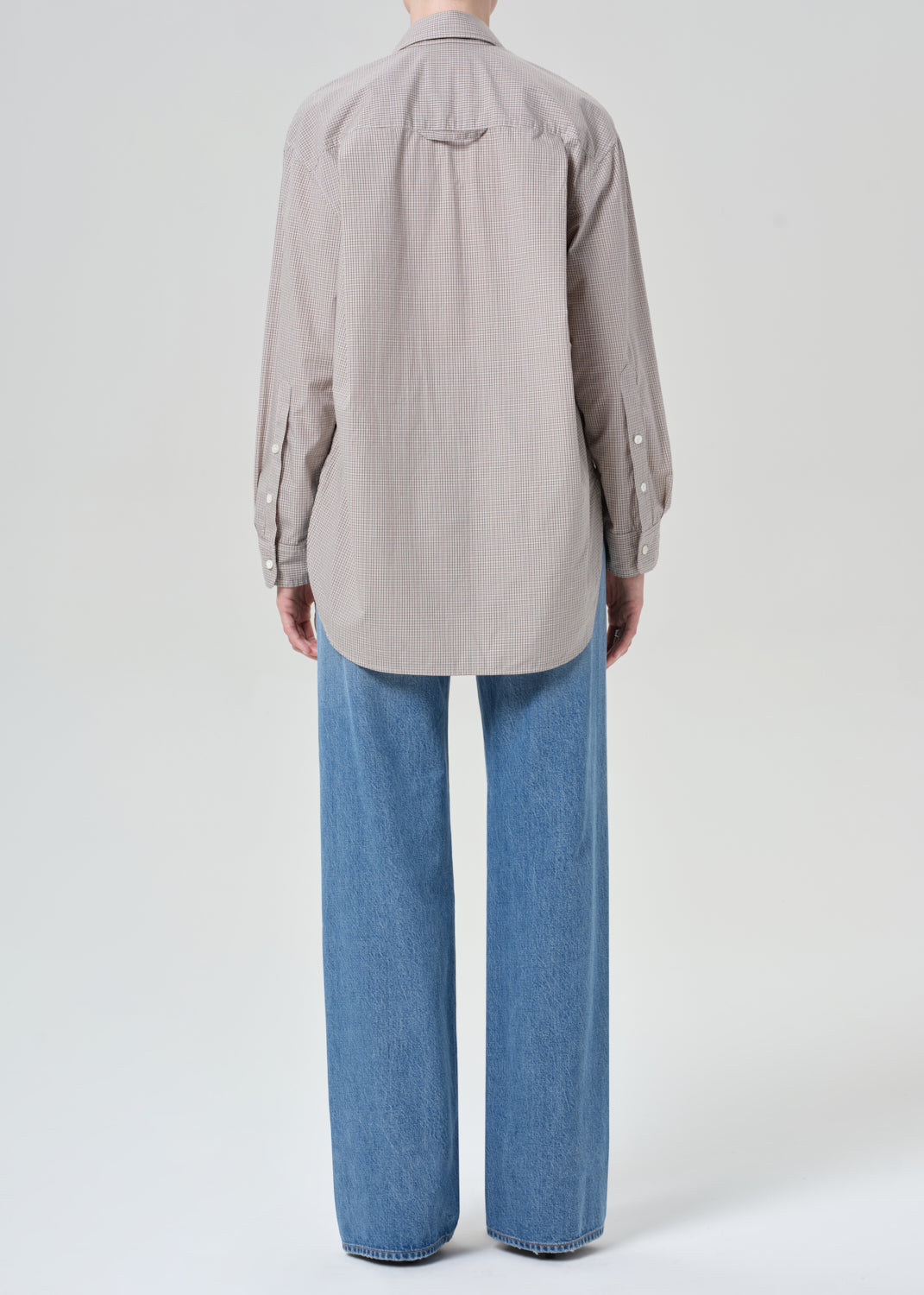 Person wearing a button-up shirt and blue jeans on a grey background