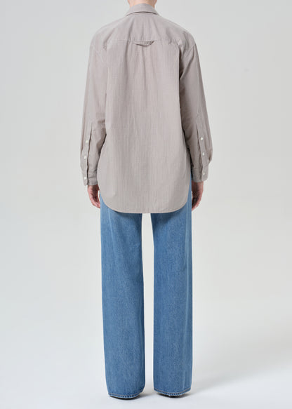 Person wearing a button-up shirt and blue jeans on a grey background