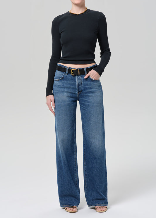 Person wearing a black long-sleeve top and blue jeans on a plain background