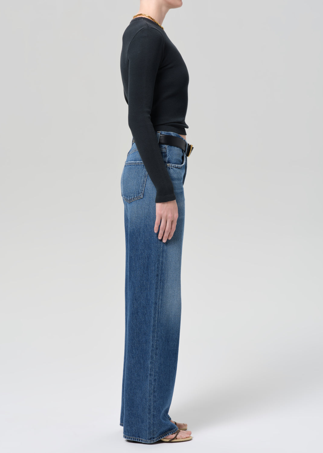 Person wearing a black long-sleeve top and blue jeans on a plain background