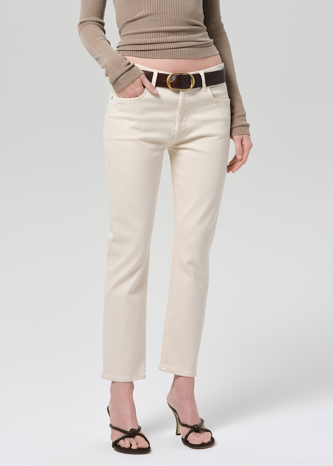 Person wearing a brown ribbed top and off-white jeans on a grey background