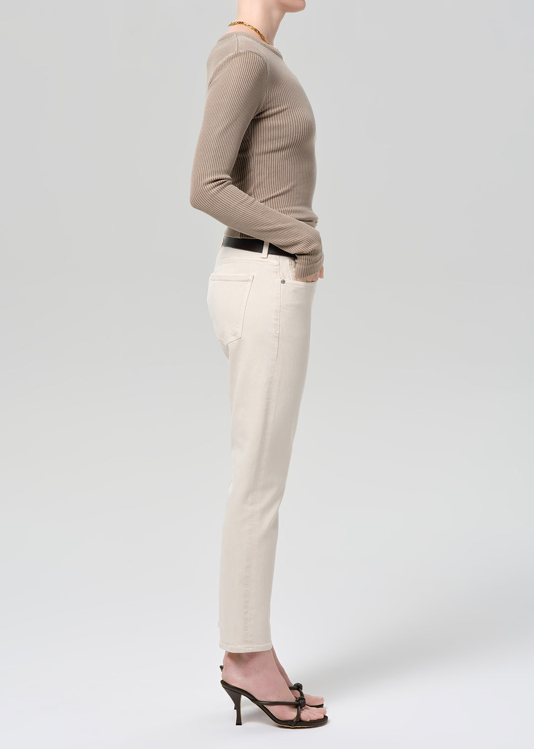 Person wearing a brown ribbed top and off-white jeans on a grey background