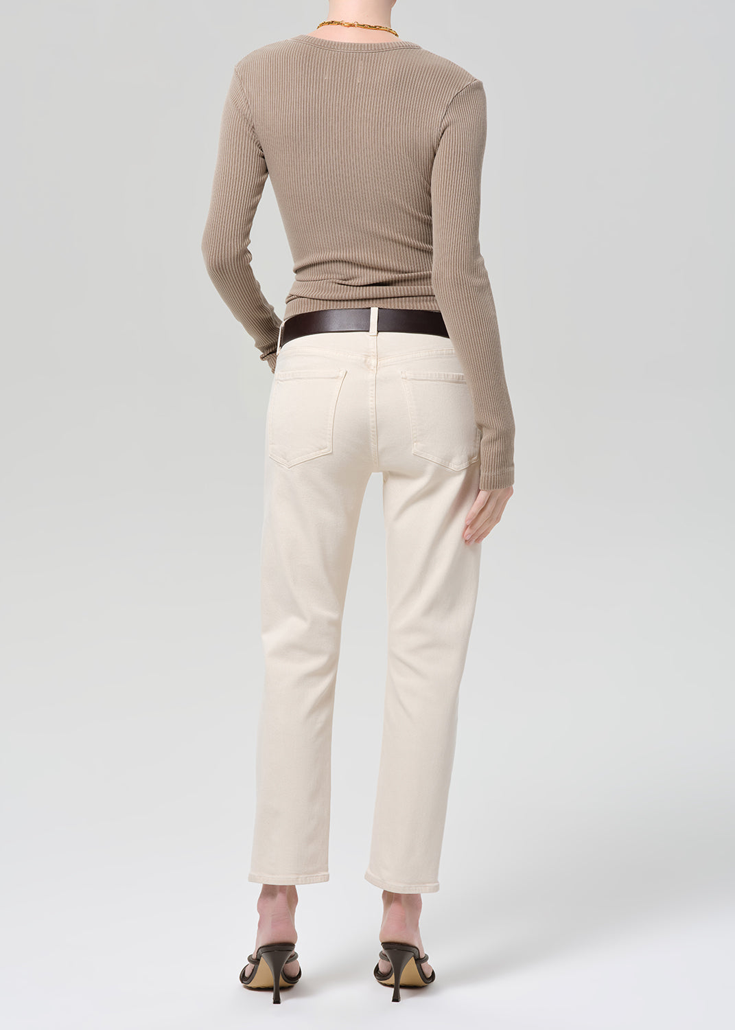 Person wearing a brown ribbed top and off-white jeans on a grey background