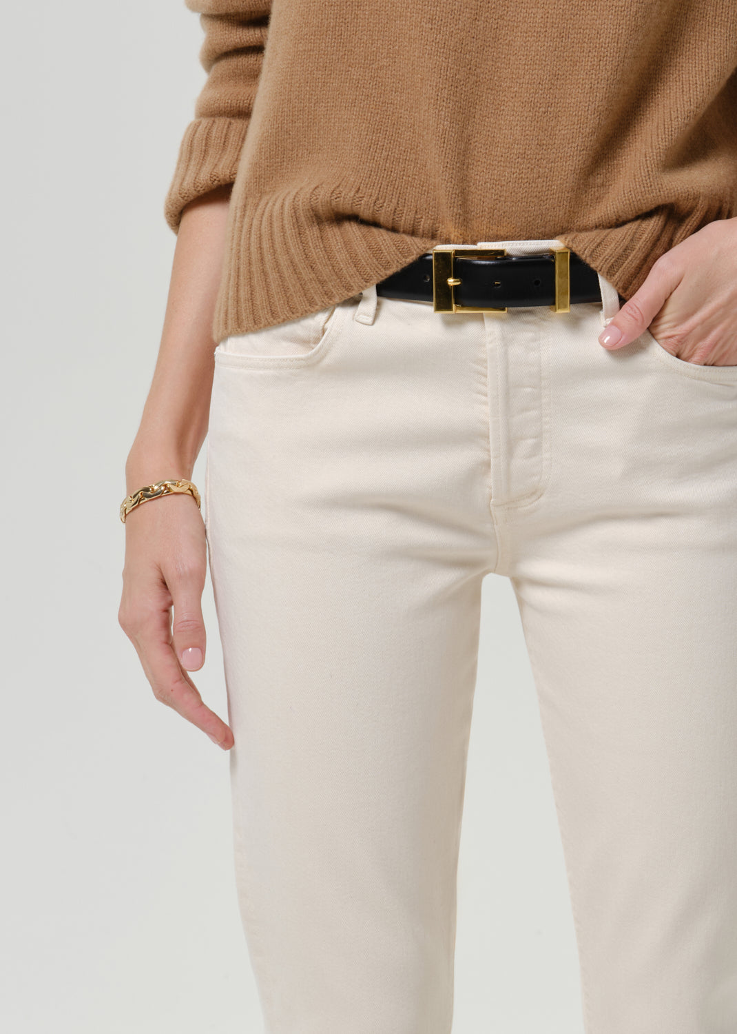 Close-up of cream straight leg jeans showing the waistband, front pockets, and black belt with gold buckle.