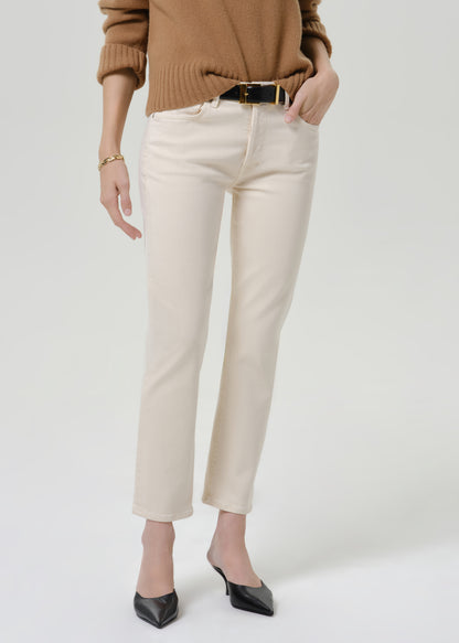 Person wearing cream straight leg cropped jeans with a camel brown crewneck sweater and black heels, front cropped view on a grey background.