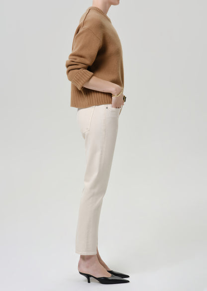 Person wearing cream straight leg cropped jeans with a camel brown crewneck sweater and black heels, side full body view on a grey background.