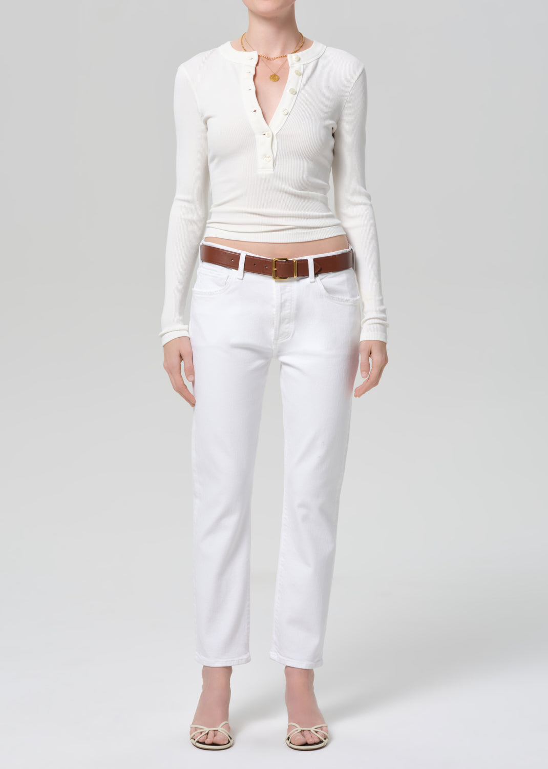 Person wearing a white long-sleeve top and white jeans with a brown belt on a light gray background