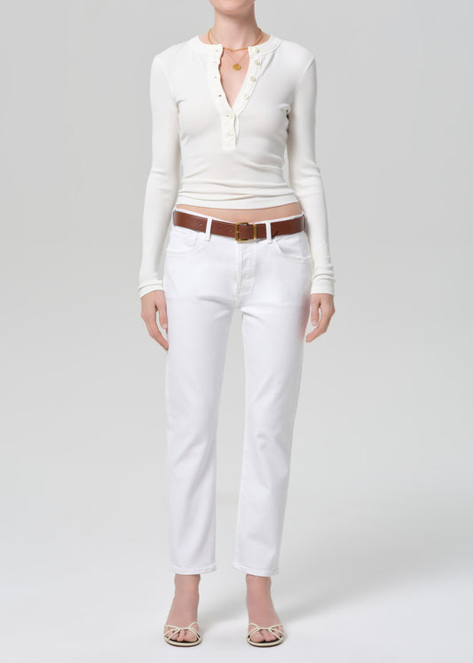 Person wearing a white long-sleeve top and white jeans with a brown belt on a light gray background