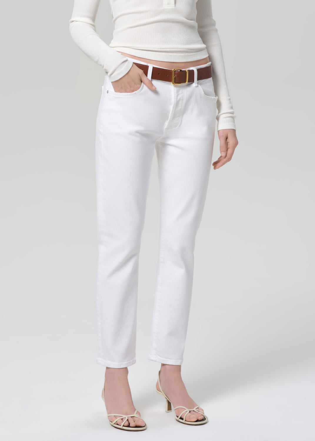 Person wearing a white long-sleeve top and white jeans with a brown belt on a light gray background