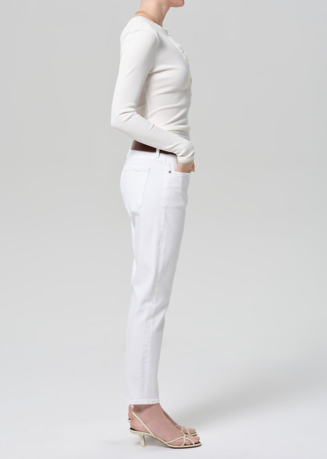 Person wearing a white long-sleeve top and white jeans with a brown belt on a light gray background