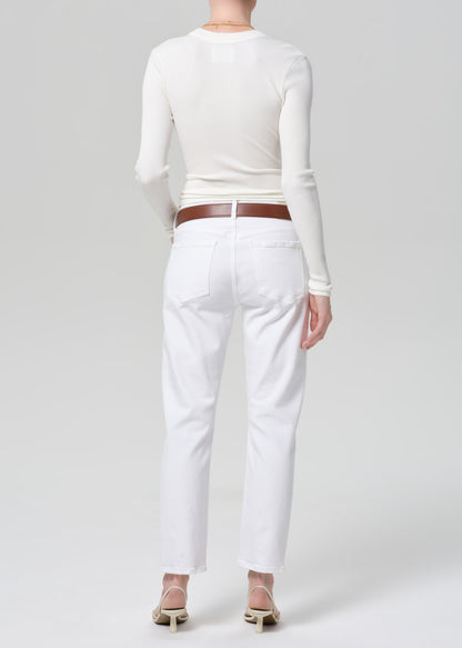 Person wearing a white long-sleeve top and white jeans with a brown belt on a light gray background