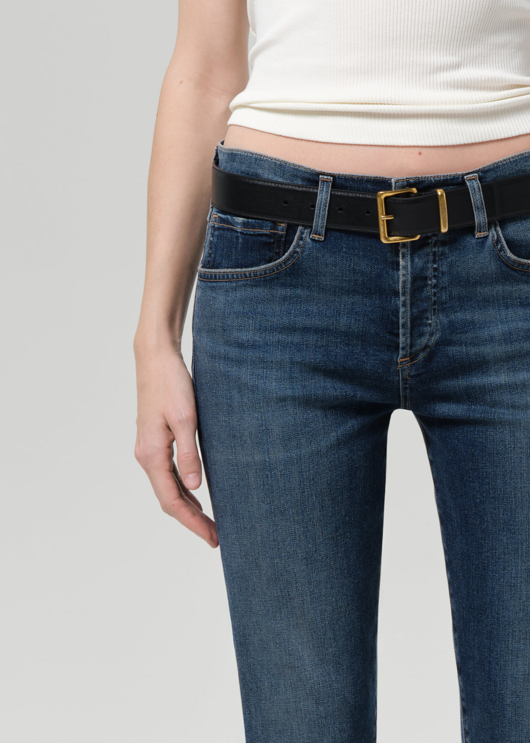 Person wearing blue jeans with a black belt on a light gray background