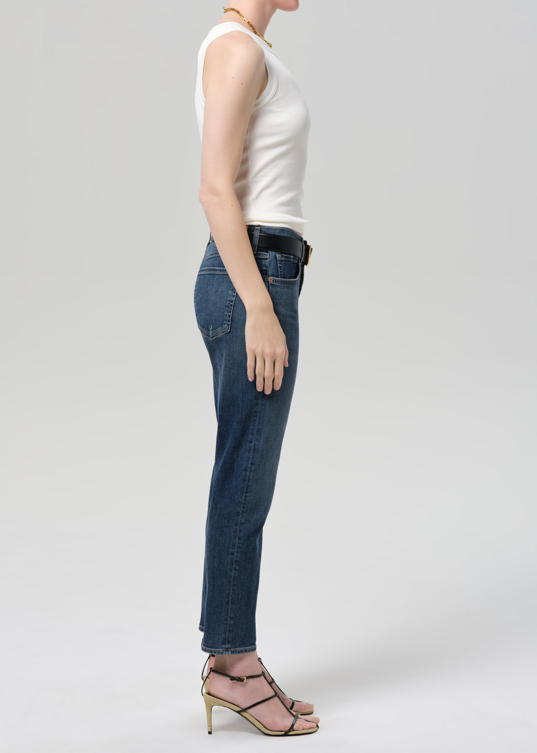 Person wearing blue jeans and a white top on a plain background