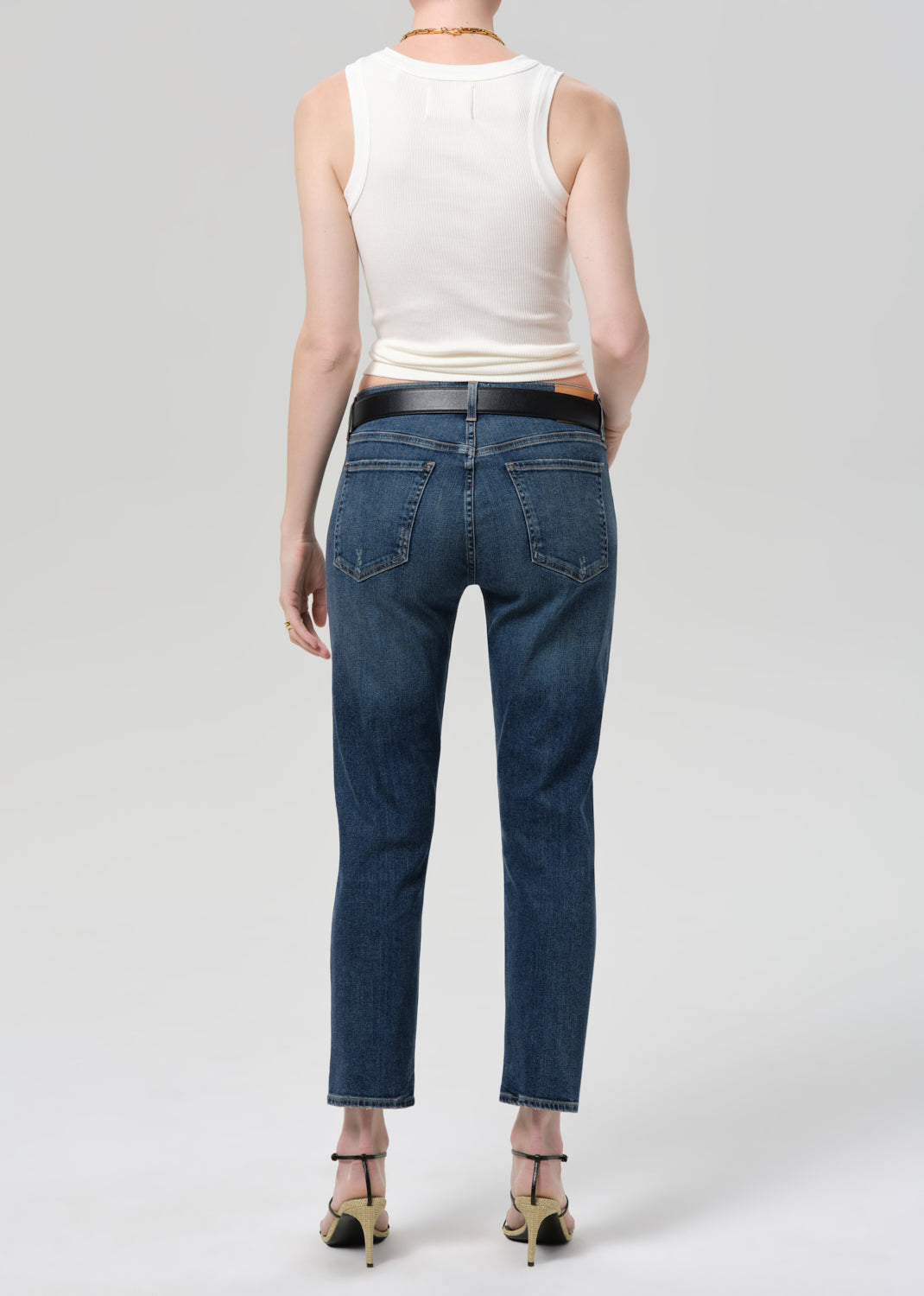 Person wearing blue jeans and a white sleeveless top on a plain background