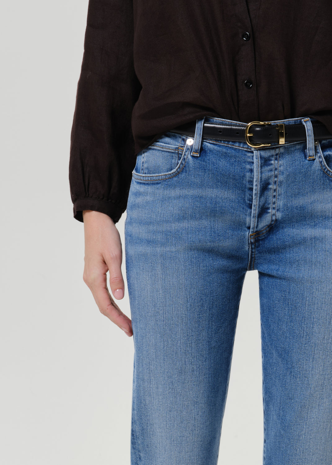 Close-up of medium blue straight leg jeans showing the waistband, front pockets, subtle fading, and black belt with gold buckle.
