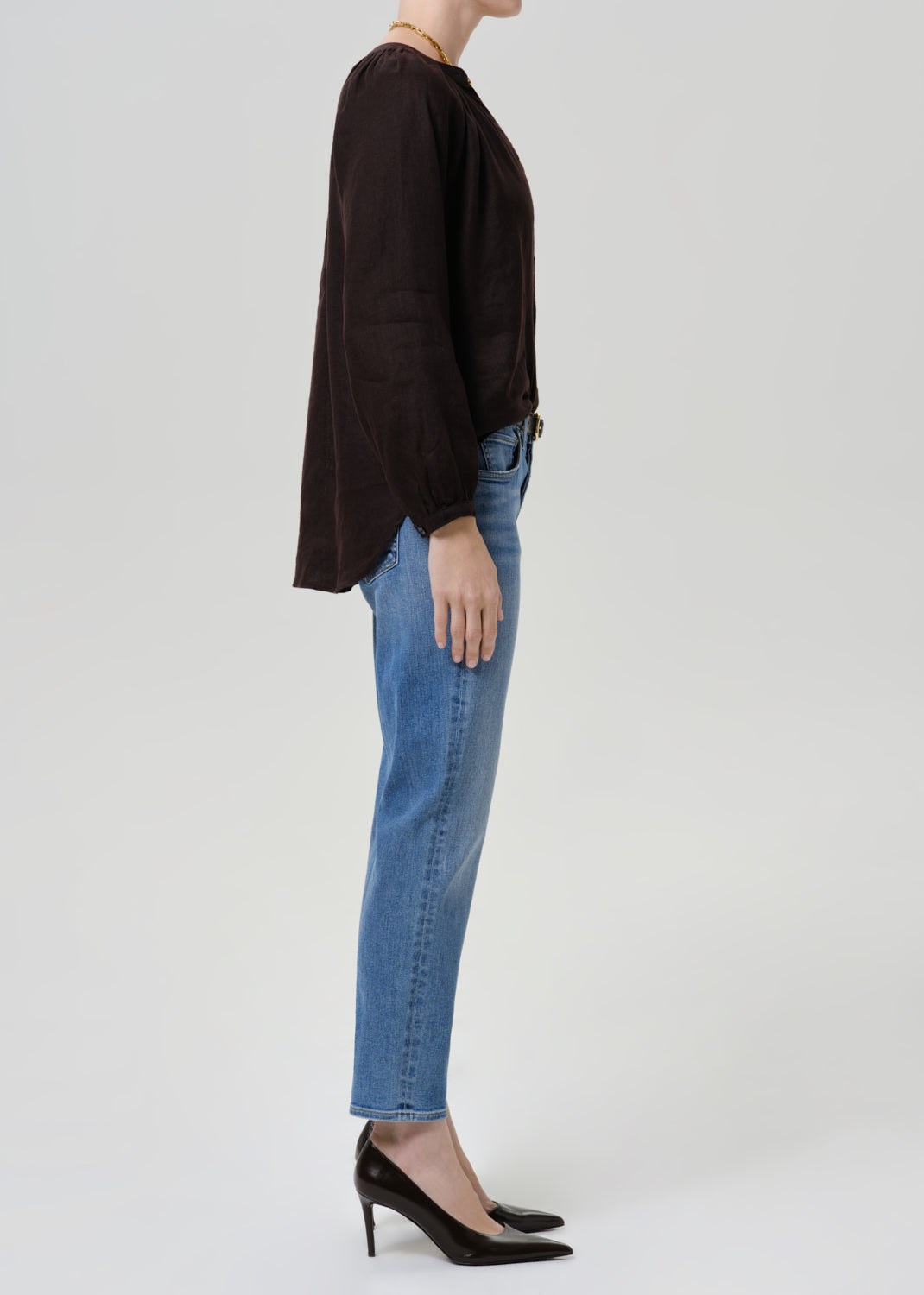 Person wearing medium blue straight leg cropped jeans with a black long sleeve blouse and black heels, side full body view on a grey background.