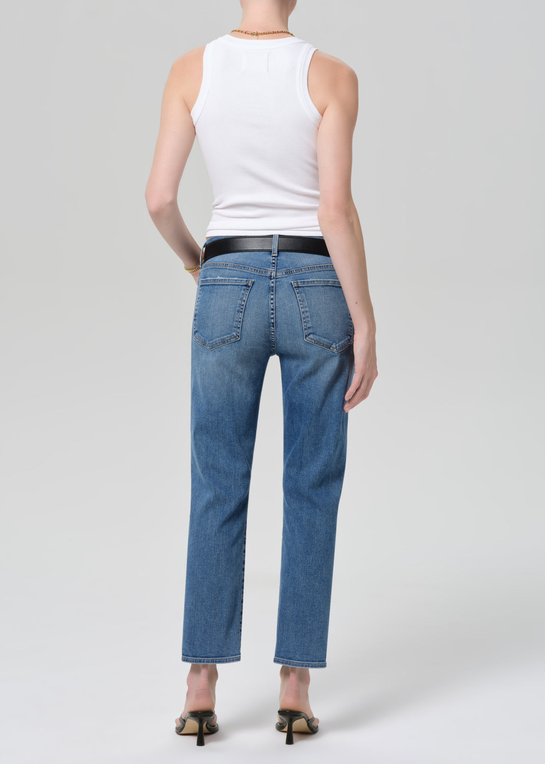 Person wearing blue jeans and a white tank top on a plain background