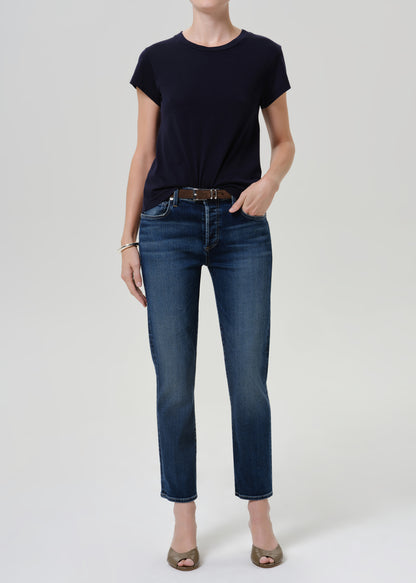 Person wearing dark blue straight leg cropped jeans with a navy short sleeve crewneck t-shirt, brown belt, and open-toe heels, front full body view on a grey background.