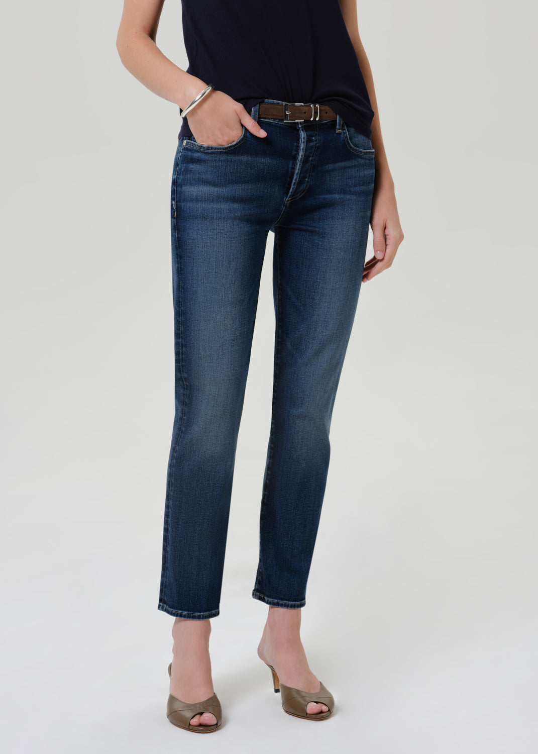 Person wearing dark blue straight leg cropped jeans with a navy short sleeve crewneck t-shirt and heels, front cropped view on a grey background.