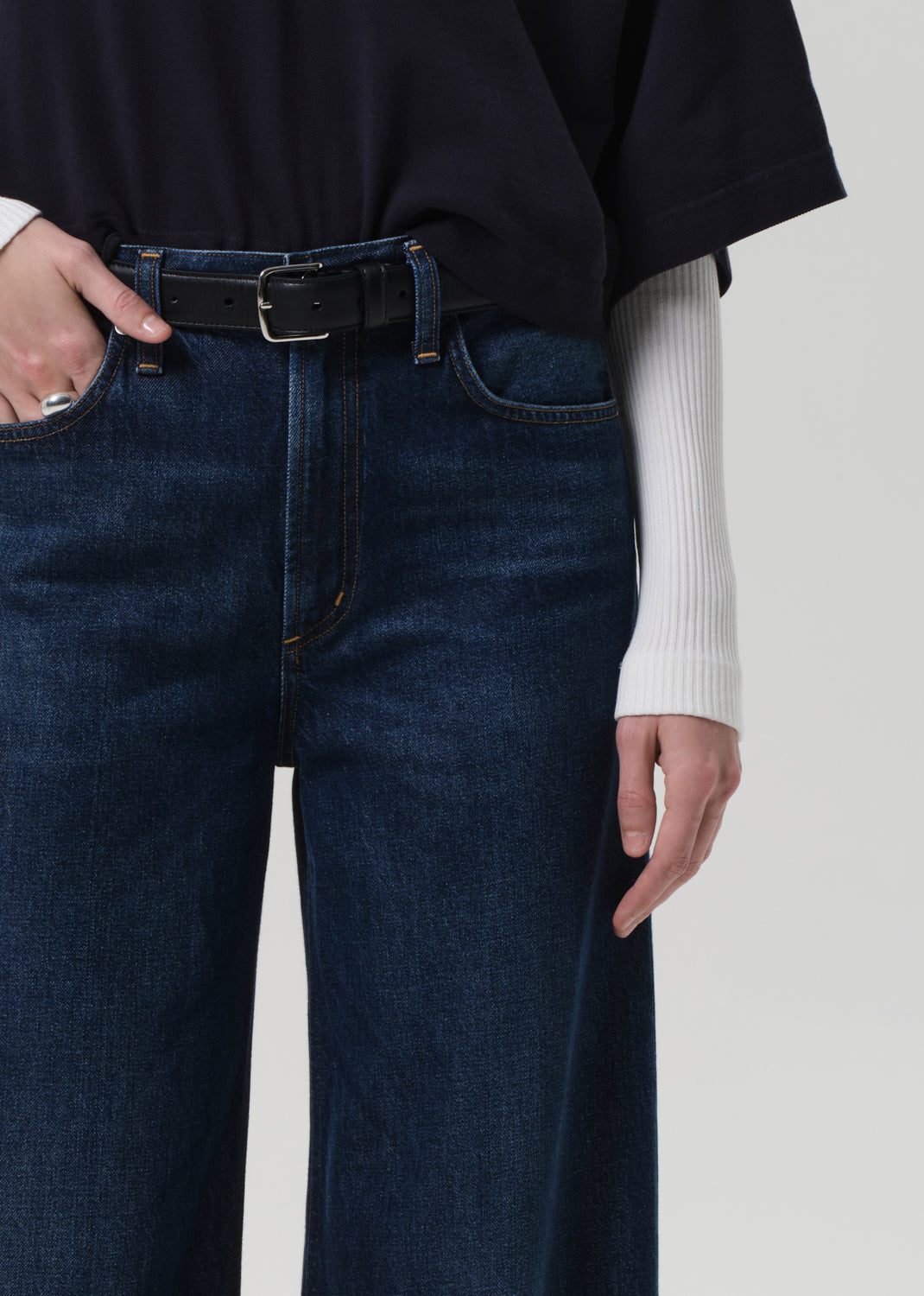 Person wearing a navy oversized polo and dark blue jeans on a white background
