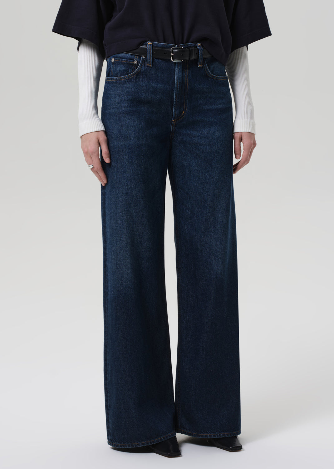 Person wearing a navy oversized polo and dark blue jeans on a white background